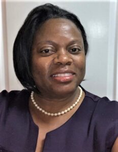 A woman with short hair wearing pearls and purple shirt.