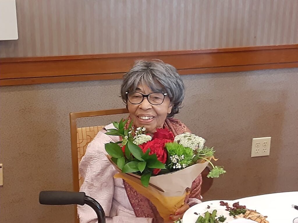 A woman sitting at the table with flowers in her lap.