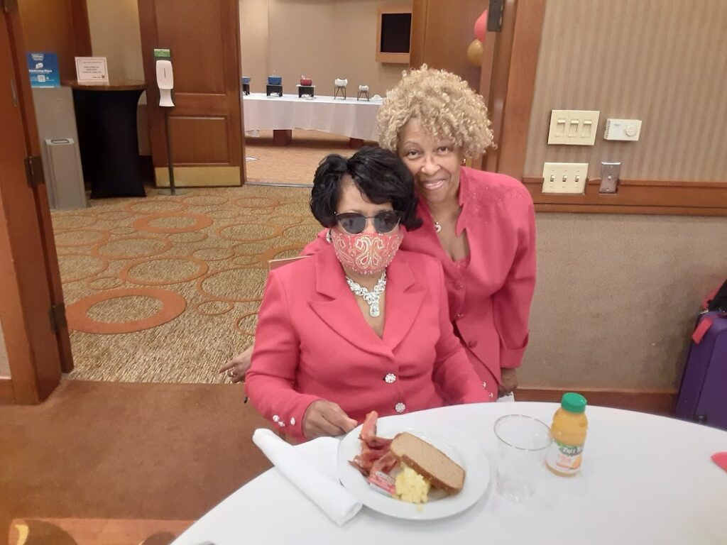 Two women in pink jackets sitting at a table with food.