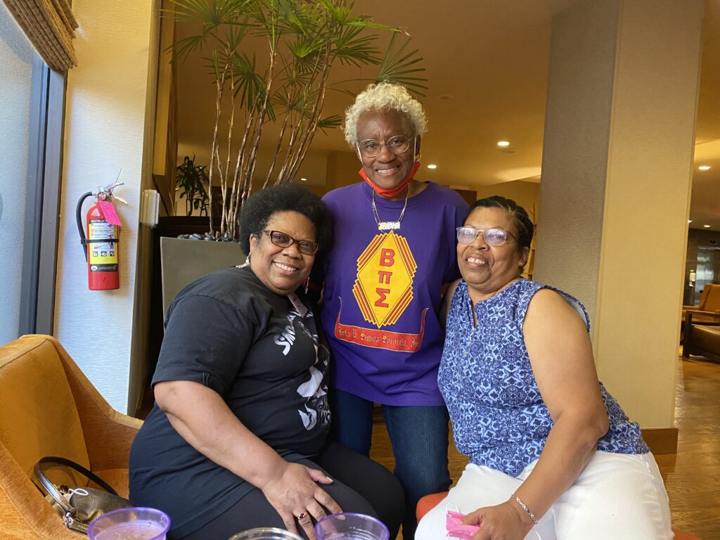 Three women pose for a picture in front of a wall.