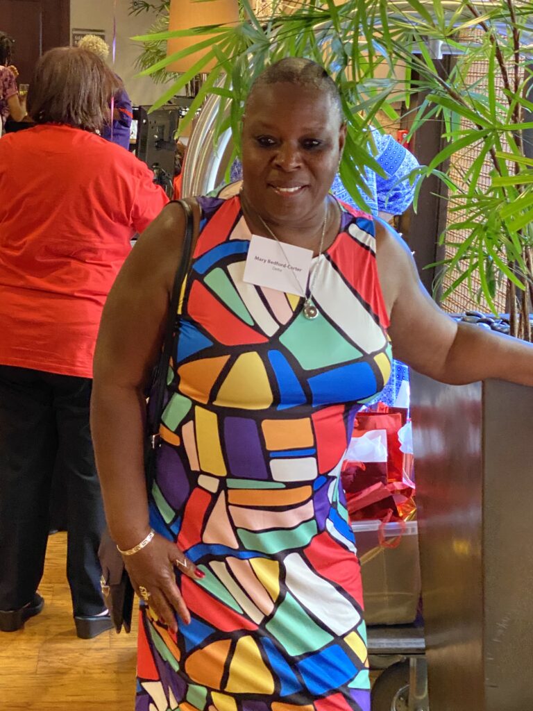 A woman in colorful dress standing next to a tree.