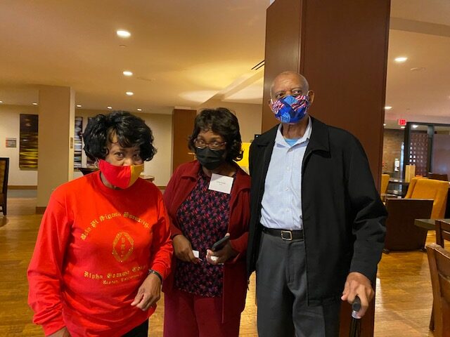 Three people standing in a room wearing masks.