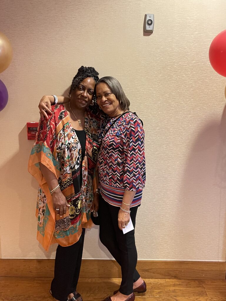 Two women posing for a picture in front of balloons.