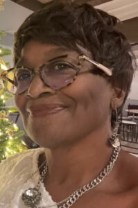 A lady with short brown hairs, smiling at the camera